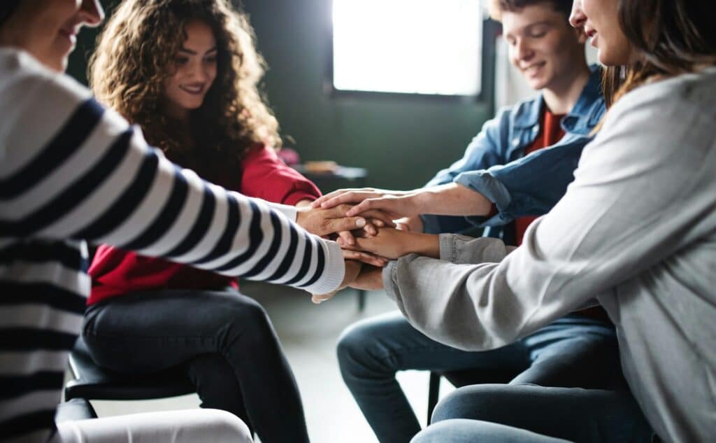men and women sitting in a circle during group therapy stacking hands together